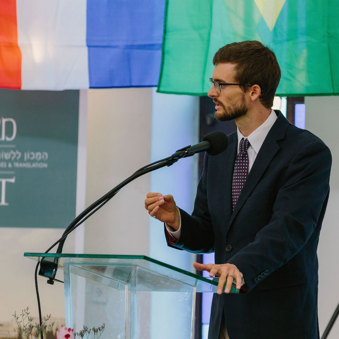 Sawyer speaking at a podium beneath a row of national flags