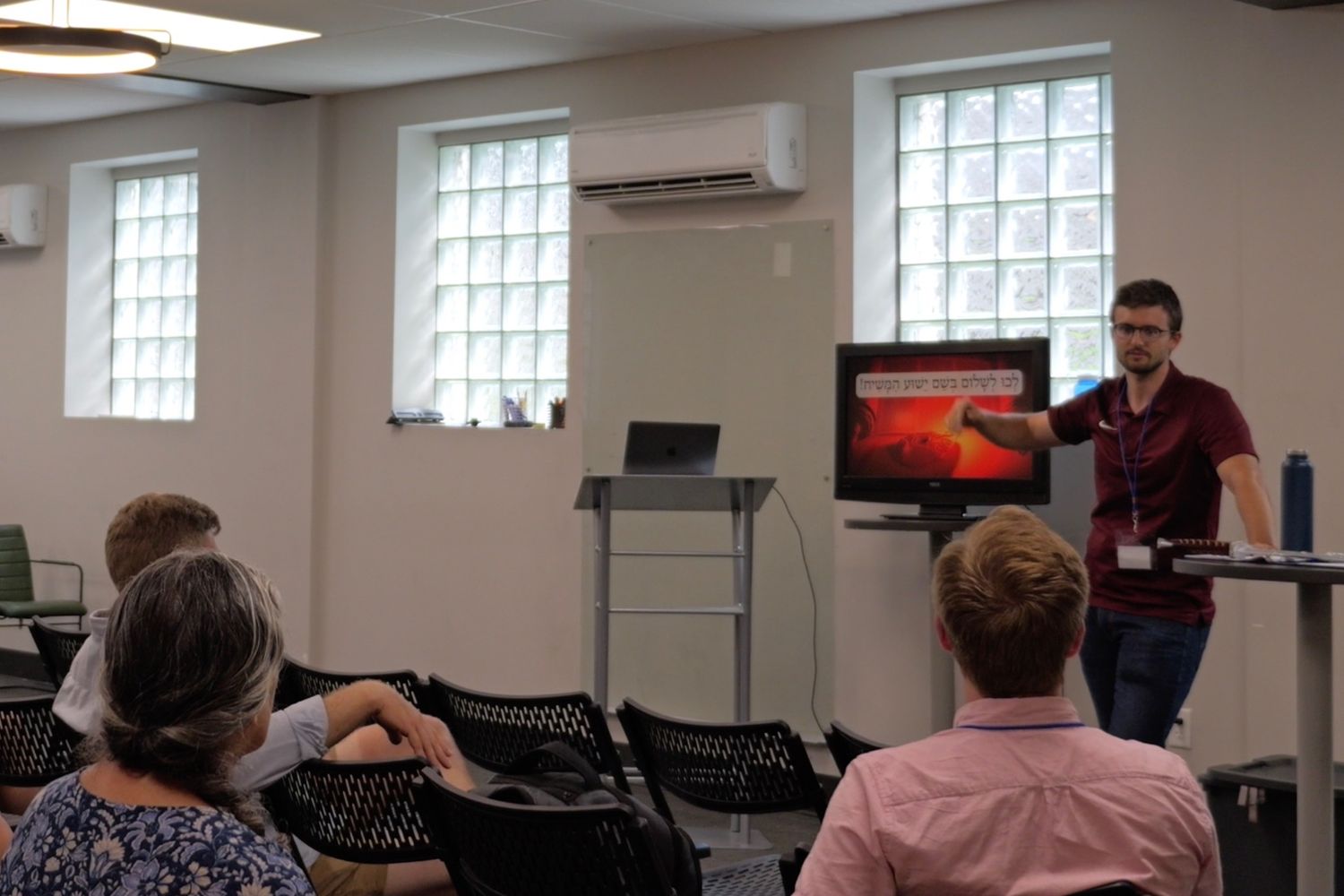 Sawyer pointing to a Hebrew sentence on a screen while teaching a room of adult students